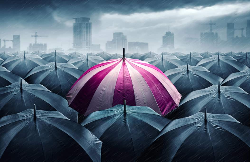Pink umbrella surrounded by dark umbrellas